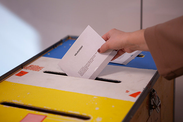 Hand lägger en valkuvert i en gul valurna.
